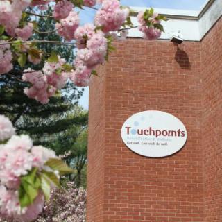 A brick building with a 'Touchpoints' sign, surrounded by blooming pink flowers.