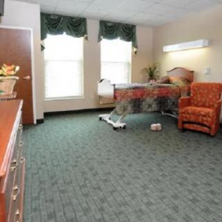 A hospital room with a bed, armchair, and large windows.