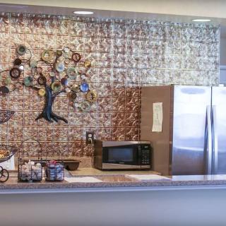 A kitchen area featuring a microwave, a large fridge, and a decorative tree sculpture on the wall.