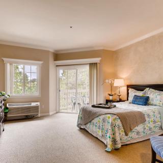A cozy bedroom with a large bed, bedside lamp, and natural light from a window and sliding door.