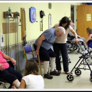 Elderly individuals receiving support and physical therapy from healthcare professionals in a rehabilitation setting.