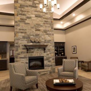 A modern living room featuring a tall stone fireplace, comfortable seating, and a stylish chandelier.