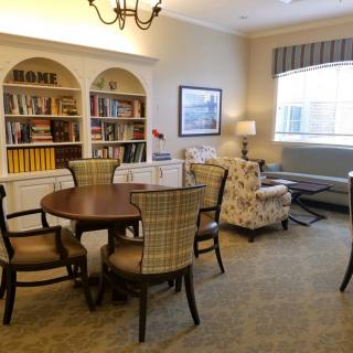 A cozy living room with bookshelves, a round table with chairs, and an armchair near the window.