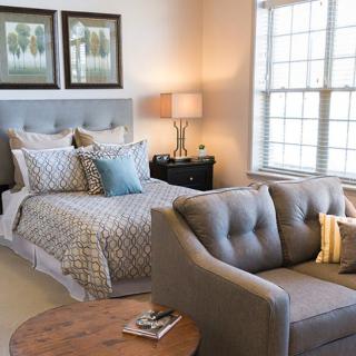 A cozy bedroom with a neatly made bed, stylish sofa, and warm lighting.