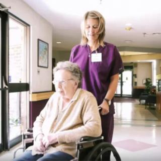 A caregiver assists an elderly person in a wheelchair in a healthcare facility.