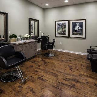 A modern hair salon interior with stylish chairs, mirrors, and framed artwork on the walls, set against a polished wooden floor.