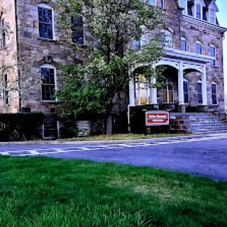 A historic stone building featuring a grand entrance and well-maintained front yard.