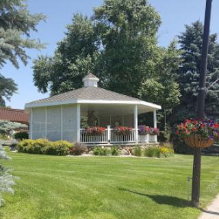 A beautifully landscaped gazebo surrounded by lush greenery and vibrant flowers on a sunny day.