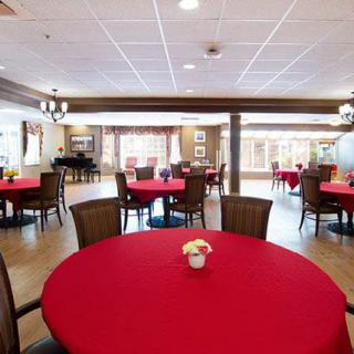 A spacious dining room with red tablecloths and a piano by the window.