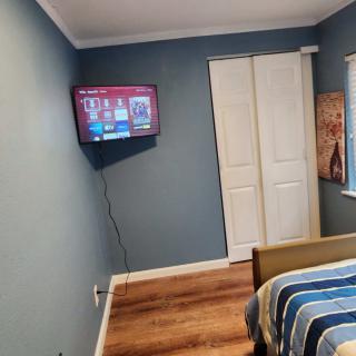 A cozy bedroom with blue walls, featuring a wall-mounted television, wooden floors, and a striped bedspread.
