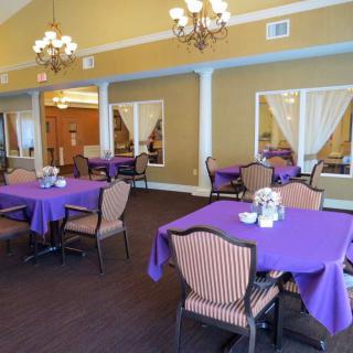 A cozy dining room featuring tables with purple tablecloths and chandeliers.
