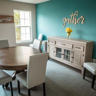 A modern dining room with a wooden table, upholstered chairs, and a sideboard, accented by wall art and a vase of yellow flowers.