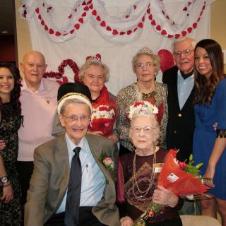 A group of elderly individuals and younger people posing together at a celebratory event with floral decorations.