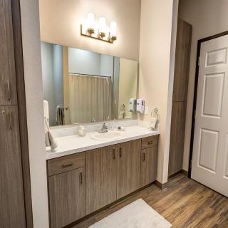 A modern bathroom with a large mirror and a wooden vanity featuring dual sinks.