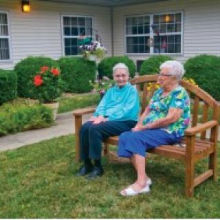 Two elderly individuals sitting on a bench in a garden, enjoying each other's company.