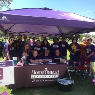 A vibrant community gathering with volunteers from Home Instead Senior Care, enjoying a sunny day under the tent.