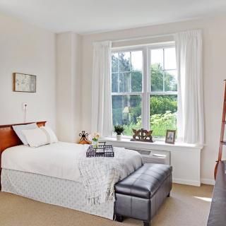 A cozy bedroom with a neatly made bed and large window allowing natural light to fill the room.