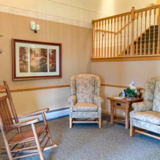 A cozy living room corner featuring a rocking chair, two armchairs, and a side table near a staircase.