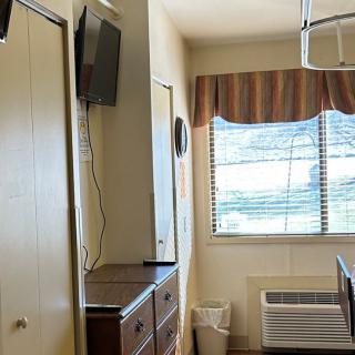 A room interior featuring a mounted television, a dresser, a window with curtains and blinds, and an air conditioning unit below the window.