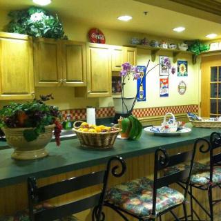 A cozy kitchen with a green countertop, bar stools, and various decorations including plants and artwork.