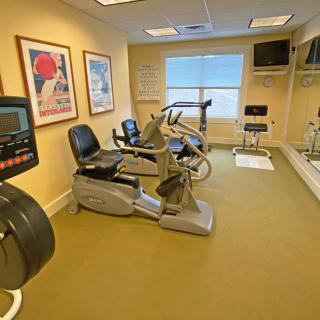 A small fitness room equipped with stationary and recumbent bikes, mirrors, and wall posters.