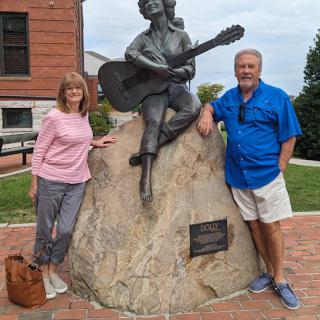 A couple posing beside a statue of a musician playing the guitar.