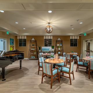 A cozy and elegantly furnished dining area featuring a grand piano, comfortable seating, and warm lighting.