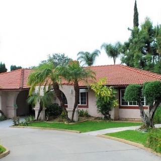 A suburban house with a red-tiled roof, surrounded by lush greenery and a curving driveway.