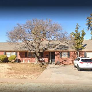 A suburban brick house with a driveway and parked car.