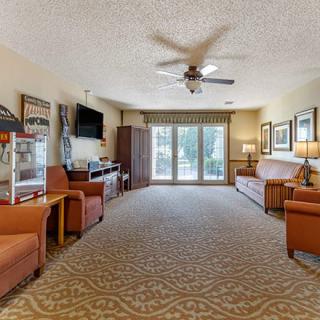 A spacious living room with comfortable seating and a television, featuring a large window and carpeted floor.