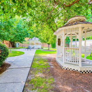 A peaceful garden setting featuring a white gazebo surrounded by lush greenery and a winding pathway.