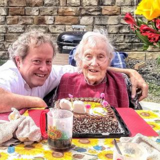 An elderly person celebrating a birthday with a cake and family outdoors.