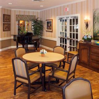 A cozy dining area with a round table and chairs, featuring elegant decor and a piano in the background.