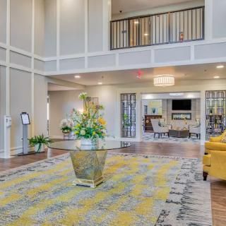 A modern lobby with elegant decor, featuring a central table with flowers, a chandelier, and comfortable seating.