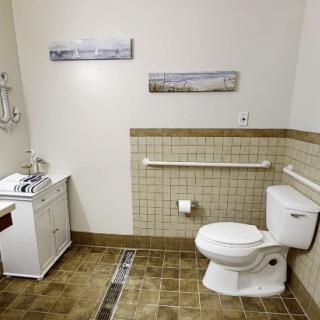 An accessible bathroom featuring a toilet with handrails, a small sink, and tiled flooring.