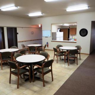 A community dining area with tables and chairs, adjacent to a kitchen.