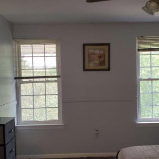 A bedroom with two windows, a dresser, and framed artwork on the wall.