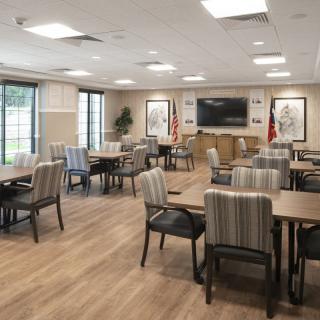 A modern dining or meeting room with neatly arranged tables and chairs, featuring a television on the wall.