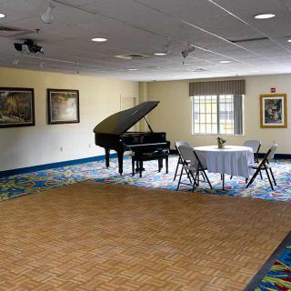 A room with a grand piano, round table, and chairs, decorated with artwork on the walls.