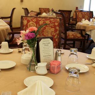 An elegantly set table in a restaurant dining room, complete with flowers and a menu.