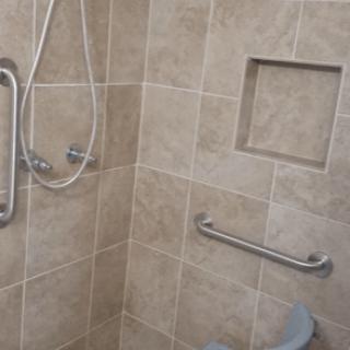 A tiled shower area with a handheld showerhead and grab bars.