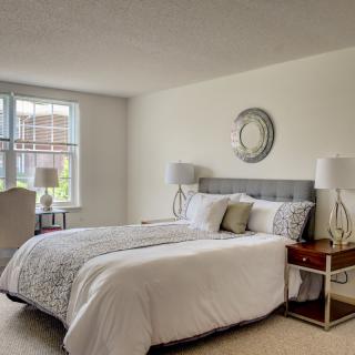 A modern bedroom with neutral tones, featuring a cozy bed, stylish nightstands with lamps, and a large window providing natural light.