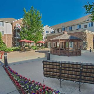 A well-maintained courtyard featuring a gazebo, benches, and flower beds under a clear blue sky.