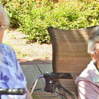 Two elderly women sitting outdoors in a garden setting.