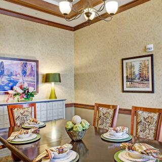A warmly decorated dining room with a set table, featuring elegant chairs and artwork on the walls.