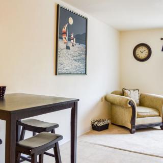 A cozy living room with a comfortable armchair, artwork on the wall, and a small table with chairs.