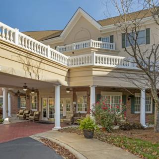 A residential building with a covered entrance and white columns, surrounded by landscaping.