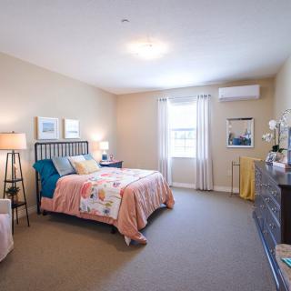 A well-decorated bedroom featuring a bed with colorful bedding, lamps, and ample natural light from the window.