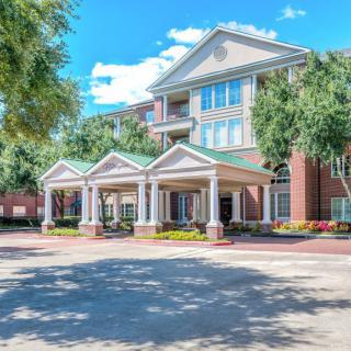A sunny day view of a hotel entrance with surrounding trees.