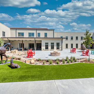 A modern building with an outdoor patio area featuring sculptures and red chairs.